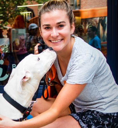 Smiling person kneeling down next to a dog on a sidewalk in New York City