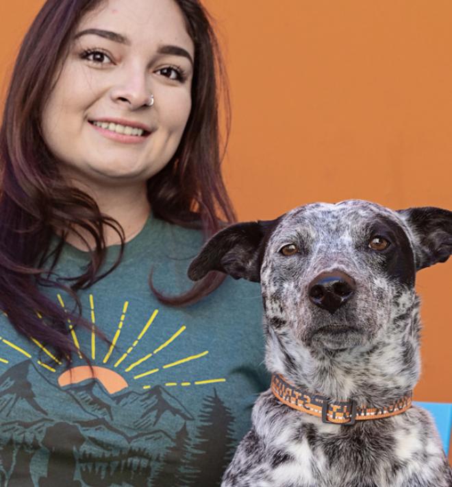 Smiling person sitting next to a black and white dog in front of an orange wall