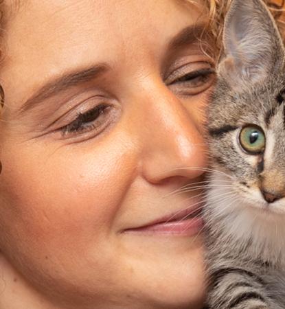 Smiling person holding a tiny kitten on their shoulder