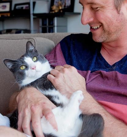Smiling person relaxing on a couch while holding a cat