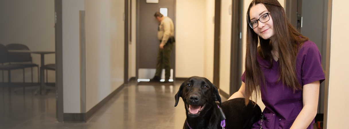 A woman in purple scrubs with a black dog