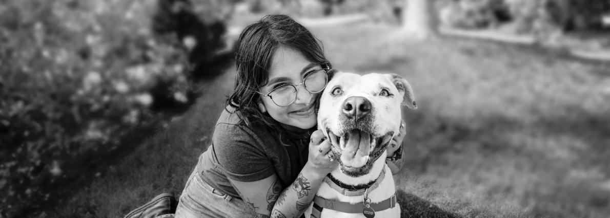 Smiling person sitting with a dog in the grass
