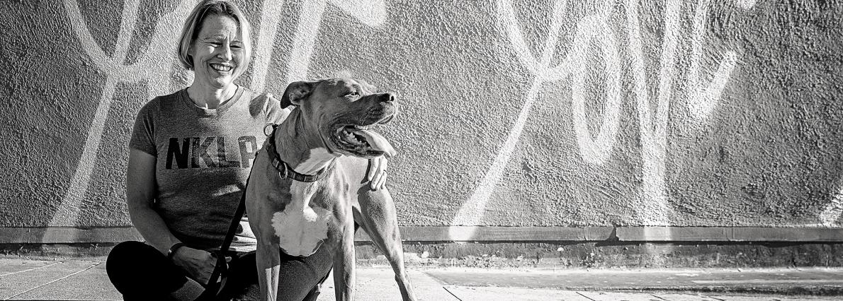 Woman with large dog sitting on sidewalk in front of mural
