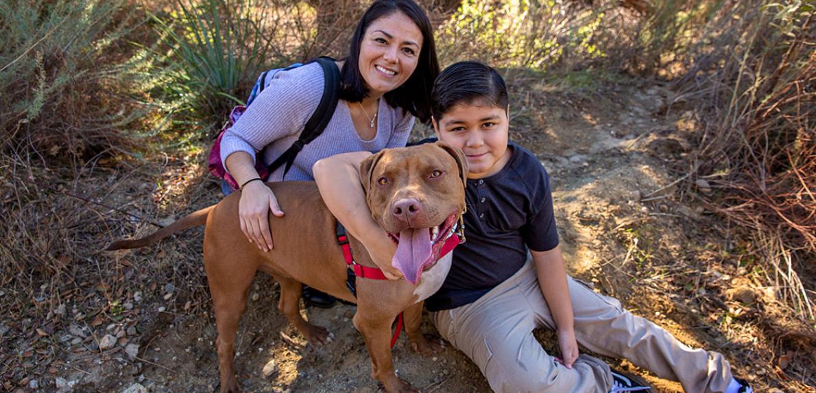 Woman and kid, outside hugging a big, brown dog