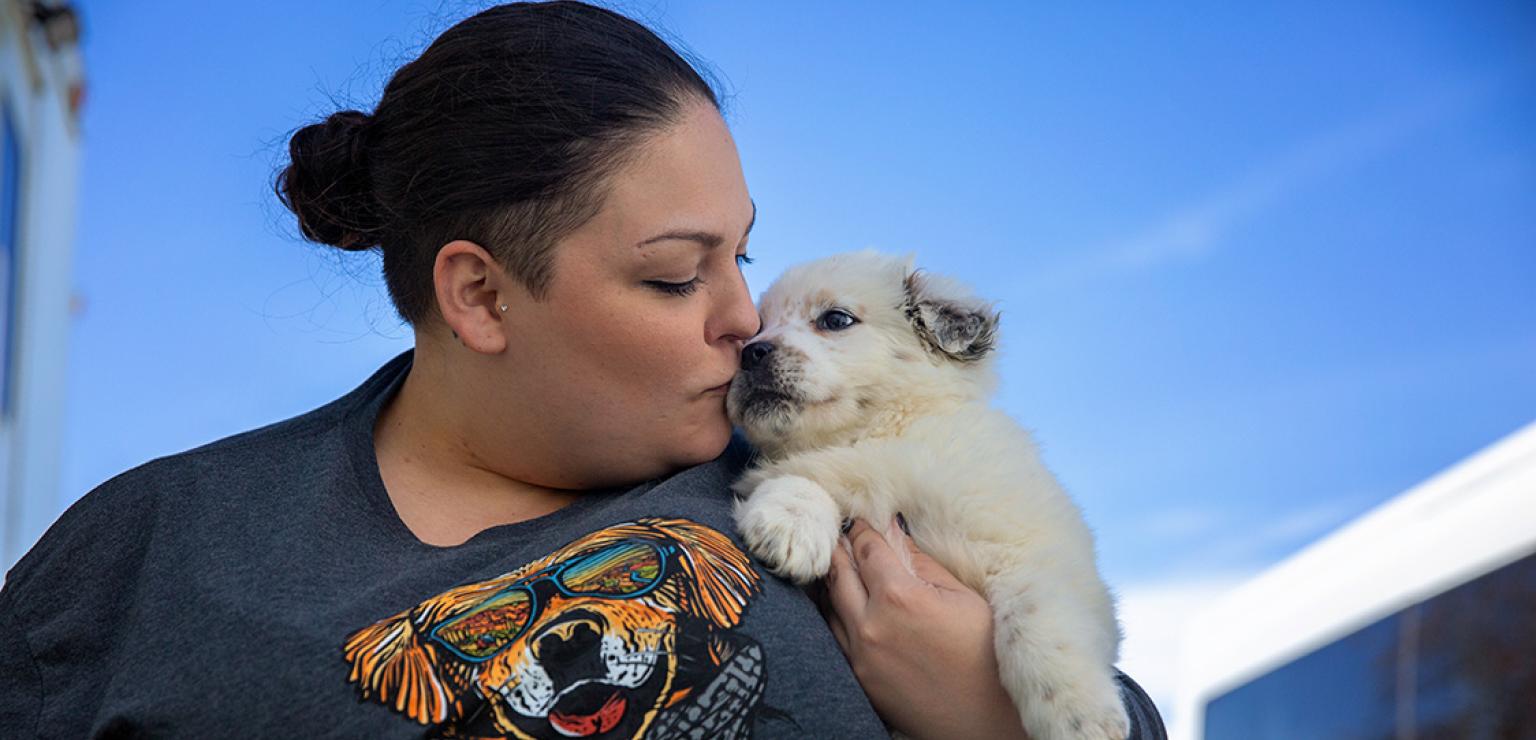 Person kissing the face of a small puppy she's holding