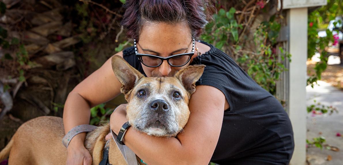 Woman hugging a brown dog with both arms wrapped around him