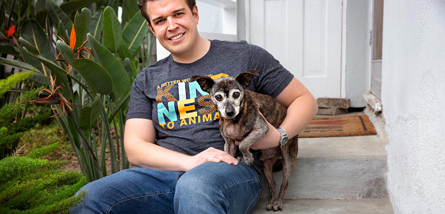 Person sitting on steps wearing a Best Friends T-shirt with an elderly dog on his lap