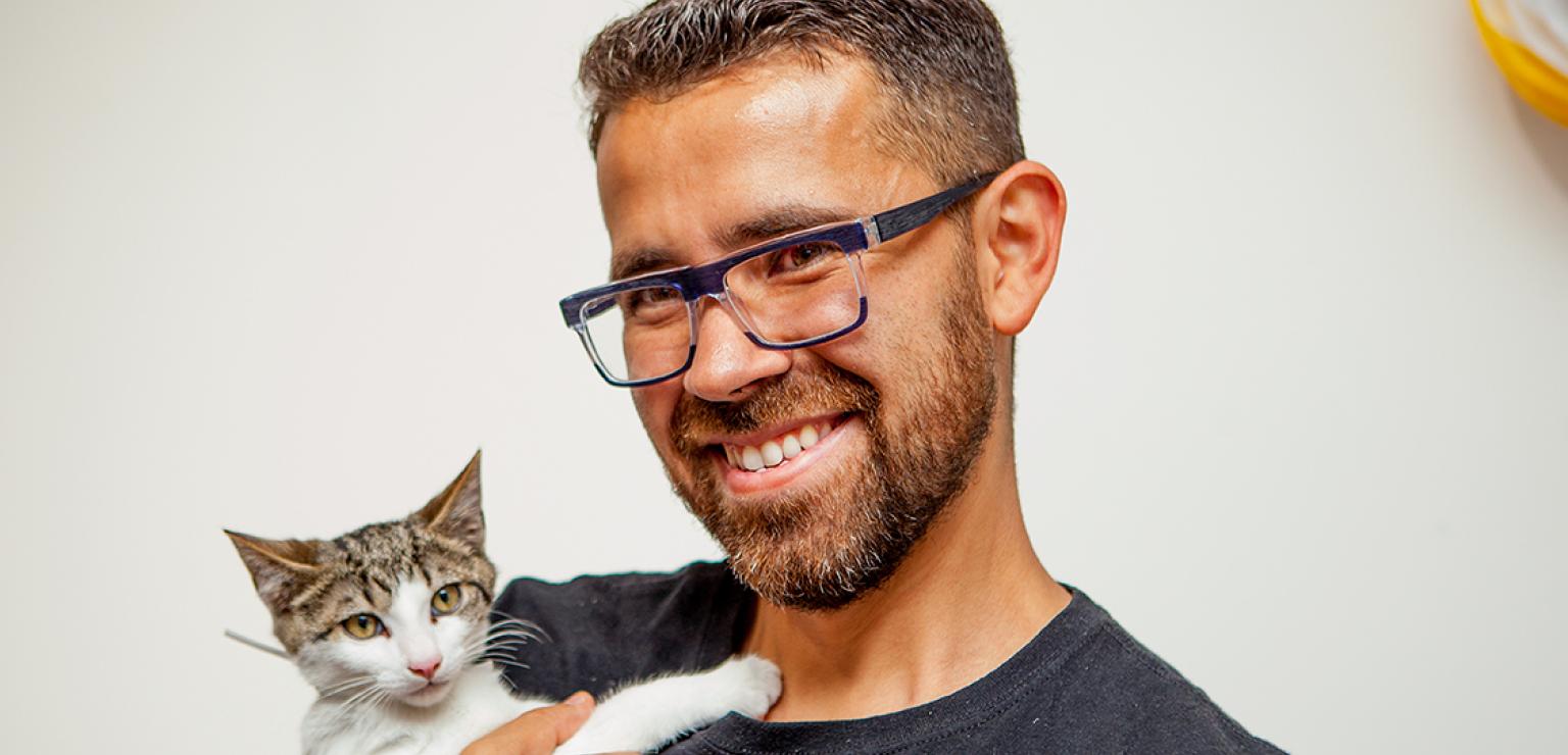 Smiling person wearing glasses holding a tabby and white cat