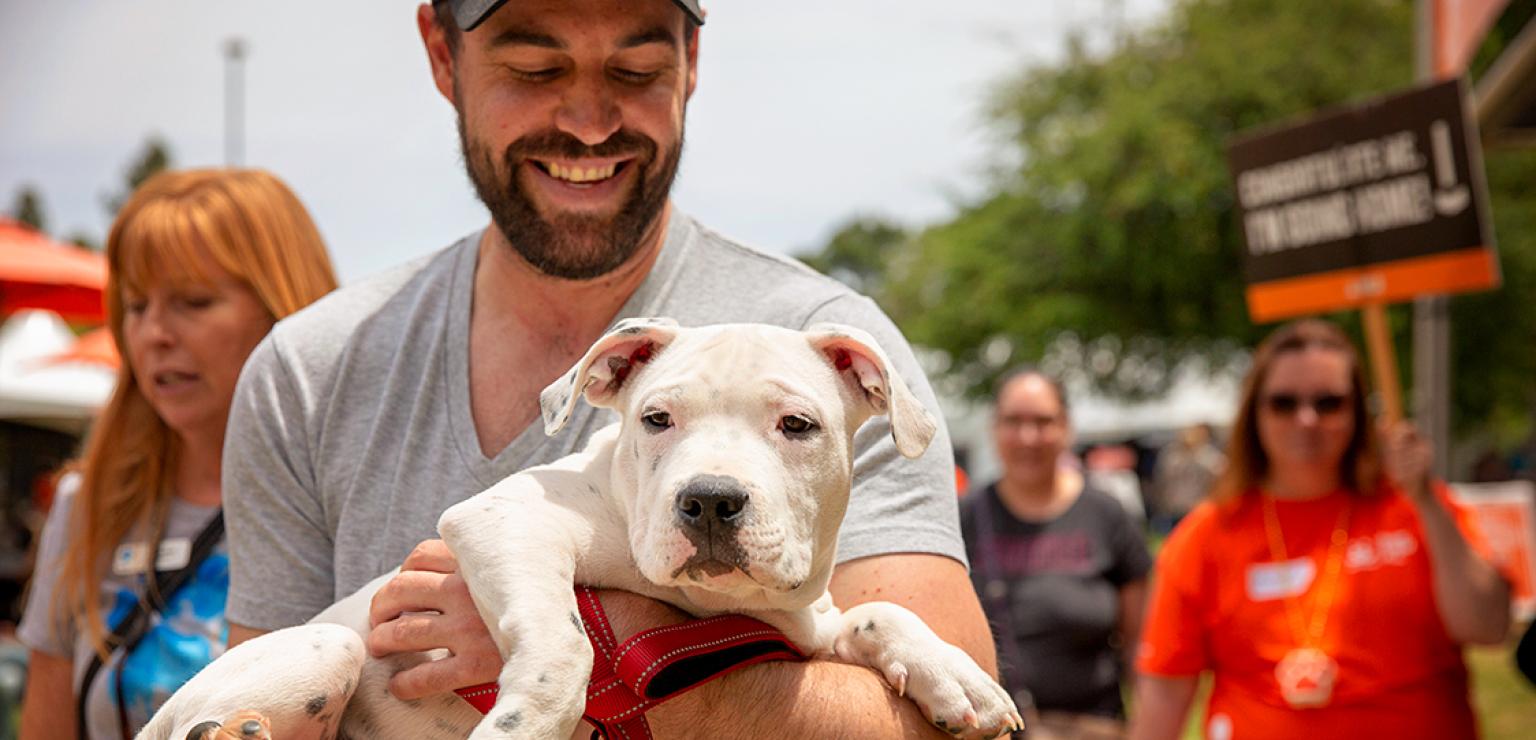 Smiling person holding a whit pit-bull-type puppy