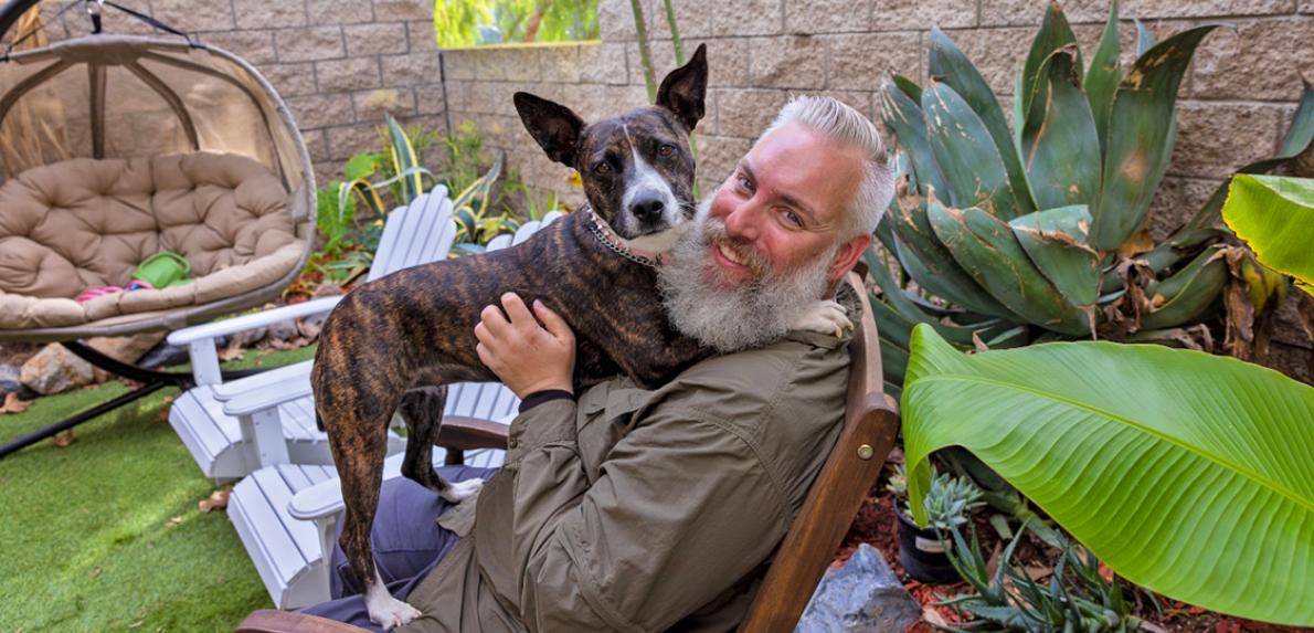 Person sitting outside in a chair with a brindle dog on his lap