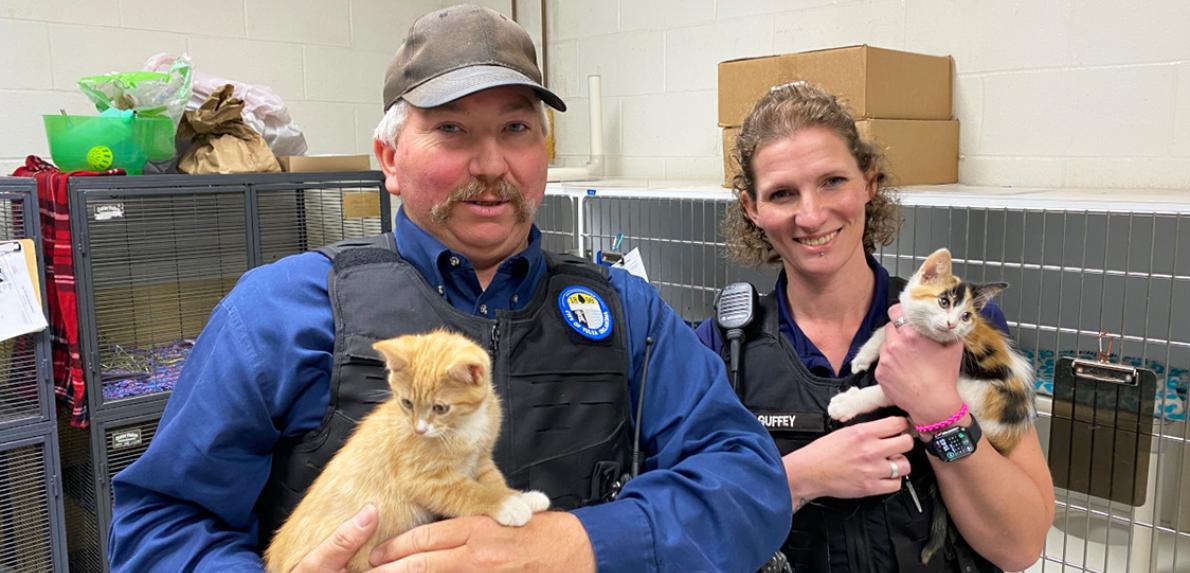 Two people in front of kennels holding kittens