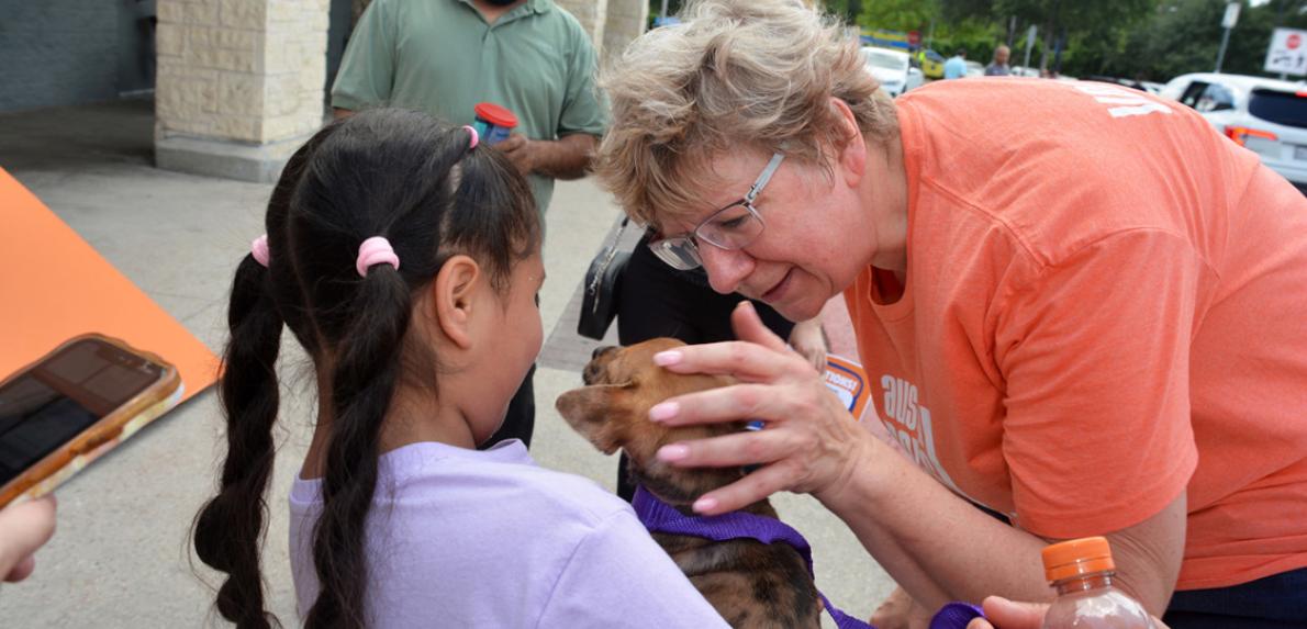 Young girl holding a puppy while an adult pets the puppy