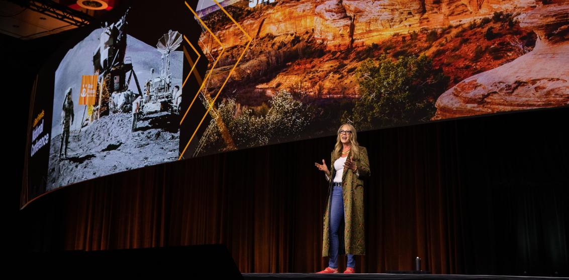 Julie Castle addressing the 2026 Best Friends National Conference attendees with giant slides of the moon landing and Angels Canyon behind her 
