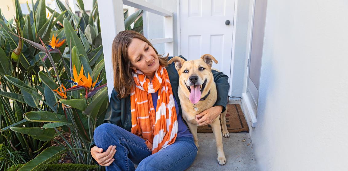 Smiling person relaxing on some steps outside of a house with a happy dog