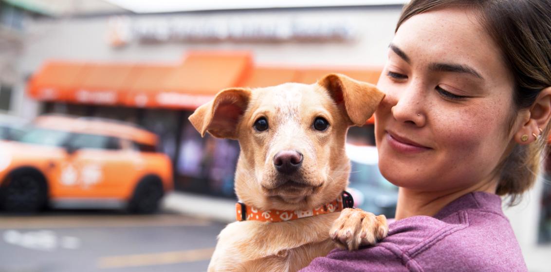 Person holding a small dog in front of a Best Friends location