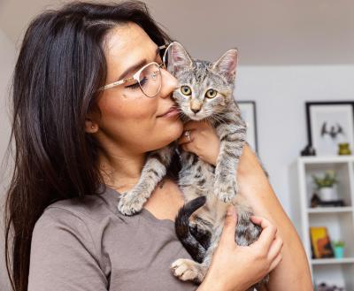 Person in a home holding a tabby cat and kissing his cheek
