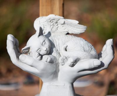 Statue of hands cupping a lying down cat with angel's wings