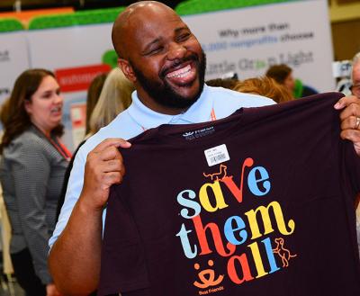 Smiling Best Friends National Conference attendee holding a Save Them All T-shirt