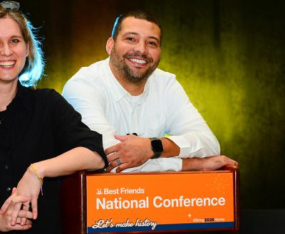 Two smiling people by a podium that says Best Friends National Conference Let's make history