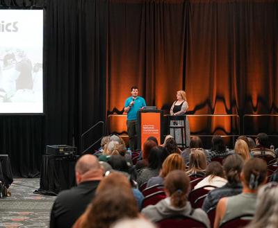 Two people presenting at the Best Friends National Conference beside a large screen featuring a spay & neuter clinic slide