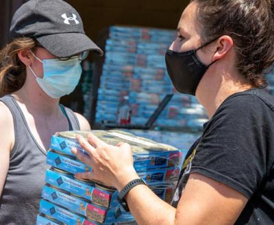 Two masked people carrying cases of canned pet food
