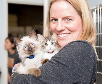Smiling person holding two kittens in front of some kennels