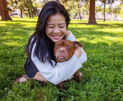 Person lying in the grass and hugging a dog, both with their eyes closed in bliss