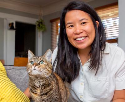 Smiling person and a tabby cat sitting on a couch in a home