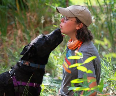 Large black dog giving a kiss to the face of a person wearing a hat