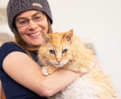 Smiling person wearing a beanie hat holding a large orange cat