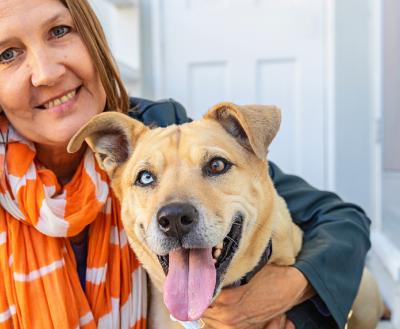 Smiling person wearing an orange and white scarf with her arm around a dog with one blue and one brown eye whose tongue is out