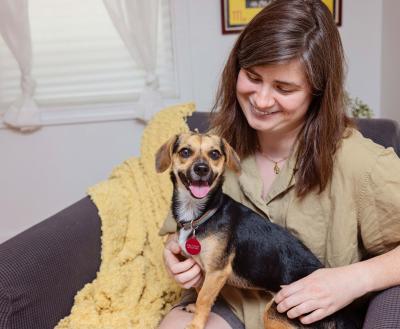 Smiling dog sitting on the lap of a smiling person sitting on a chair with a yellow blanket
