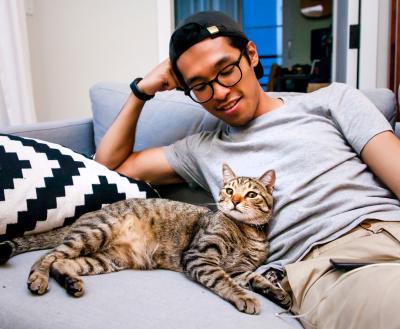 Person wearing a backward baseball hat sitting on a couch with a brown tabby cat