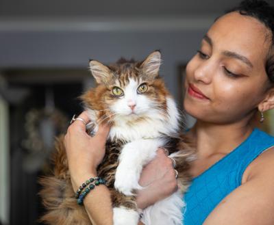 Smiling person holding a longhair tabby and white cat