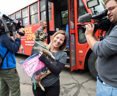 Person getting off a transport vehicle with a small dog surrounded by media cameras