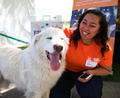 Smiling volunteer kneeling next to a happy dog at a pet adoption event in Salt Lake City