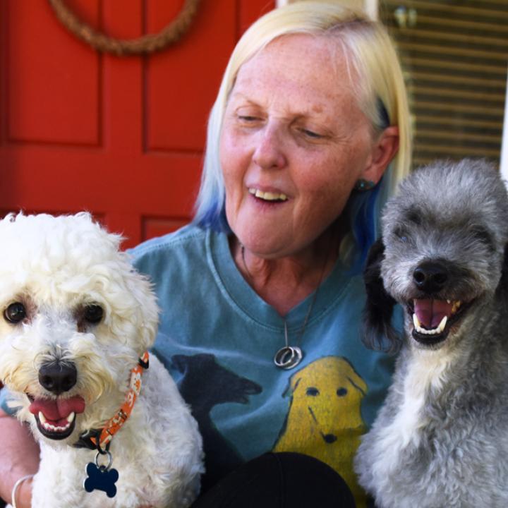 Smiling person sitting on the steps of a front porch with three dogs