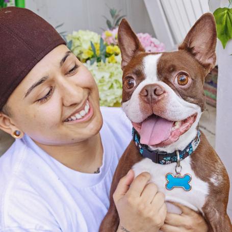 person holding brown and white, smiley, dog outside on porch