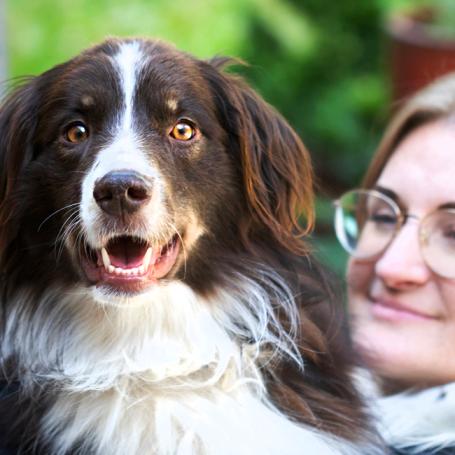 Smiling person holding a fluffy dog outside on steps leading into a house