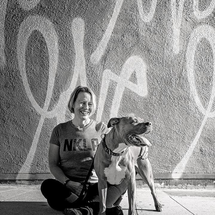 Woman with large dog sitting on sidewalk in front of mural