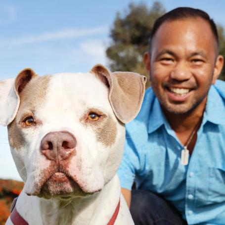 Two smiling people sitting in the grass with a big dog