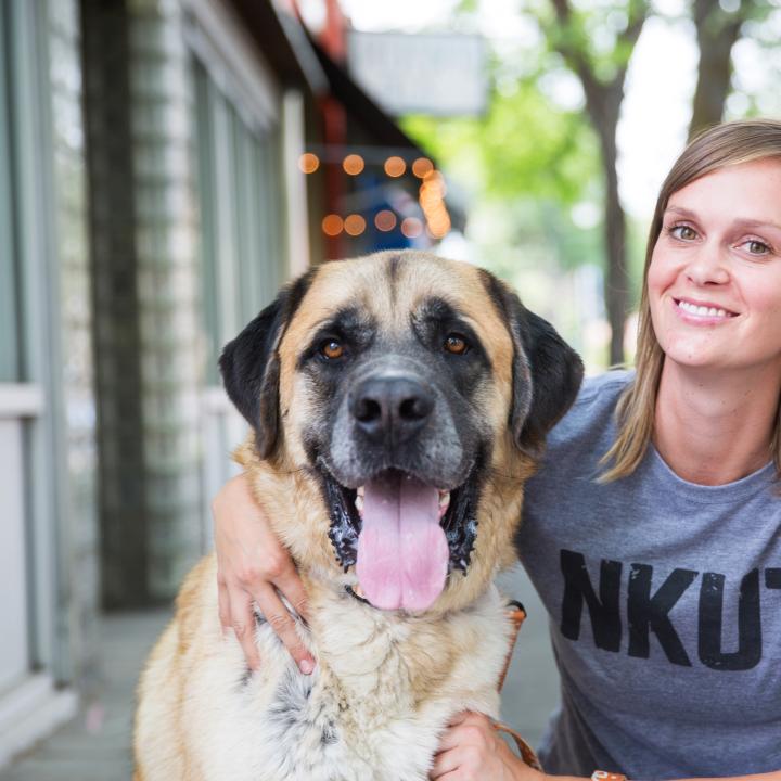 Happy dog with tongue out next to a person wearing a NKUT T-shirt