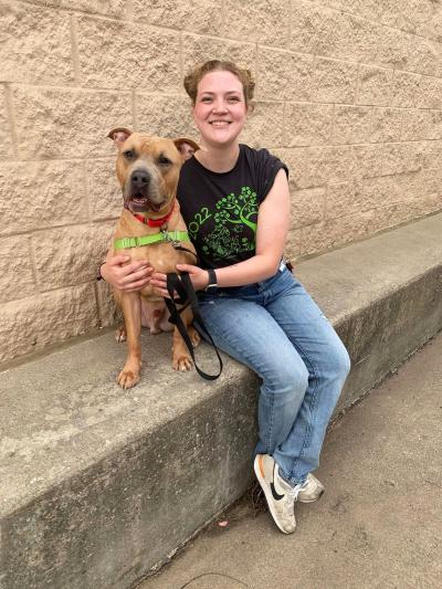 Smiling person sitting on a concrete bench next to a brown dog with her arms around him