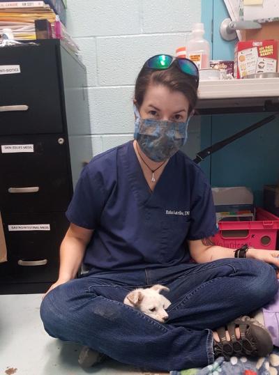 Dr. Erin Katribe wearing a mask sitting on the floor with a puppy in her lap
