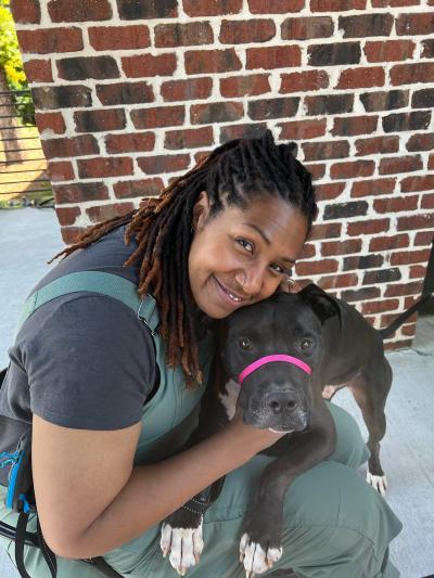 Smiling person holding a black and white pit-bull-type dog in front of a brick wall