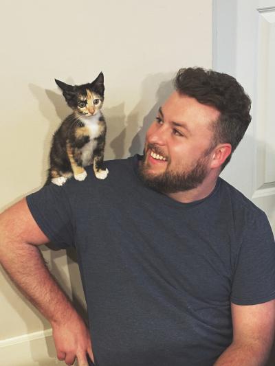 Smiling person with Arya the calico kitten sitting on his shoulder