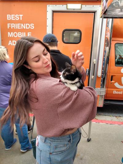 Person holding Adrian the cat in front of the Best Friends Mobile Adoption vehicle
