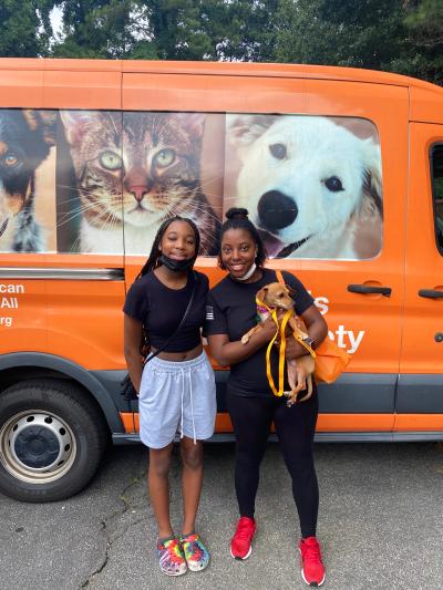 Two people holding Lady the dog in front of a Best Friends van