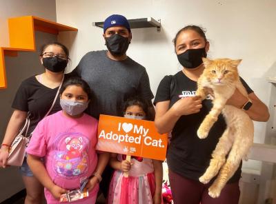 Masked family adopting Zazu the cat along with a sign that says, I heart my adopted cat