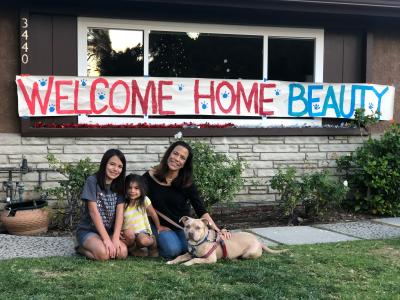 Family adopting Beauty the dog, with a big sign behind them that says, 'Welcome home Beauty'
